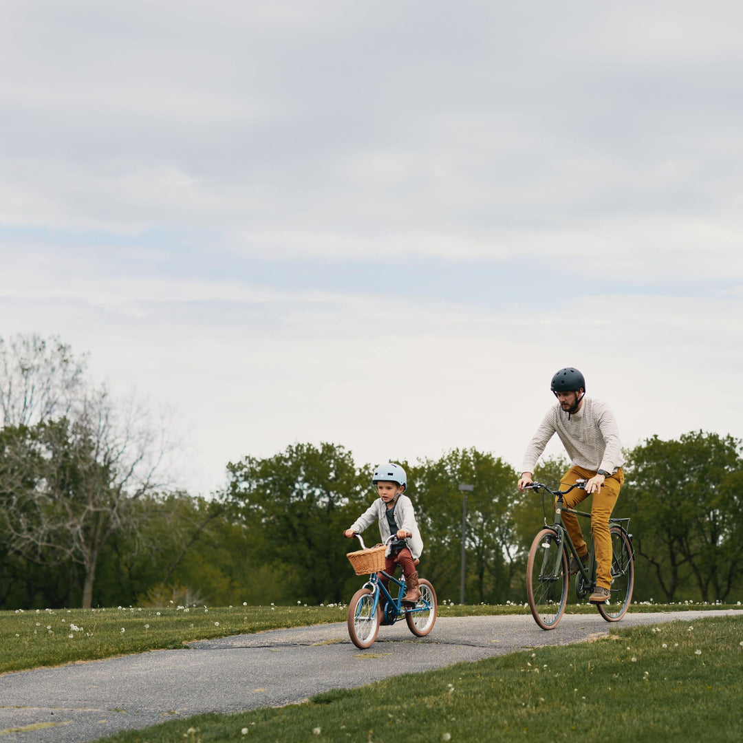 An adult and child riding bicycles on a paved path in a grassy park.