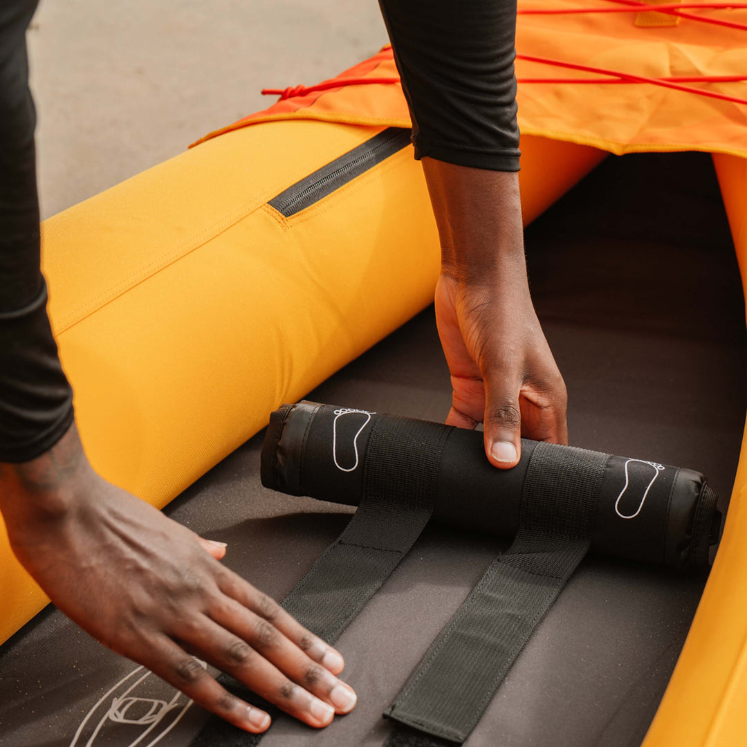 A person adjusts a black footrest on the interior of a Coaster Inflatable Kayak, focusing on securing it in place.