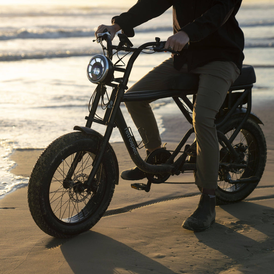 Retrospec fat tire electric bike rider navigating a sandy beach path on a sunny day.