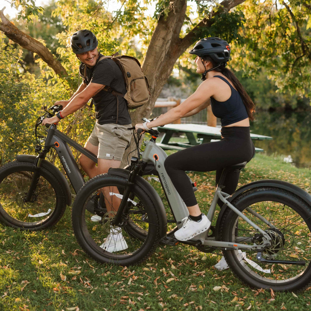 couple riding retrospec fat tire Electric Bikes through a sun-dappled park, smiling and chatting at golden hour