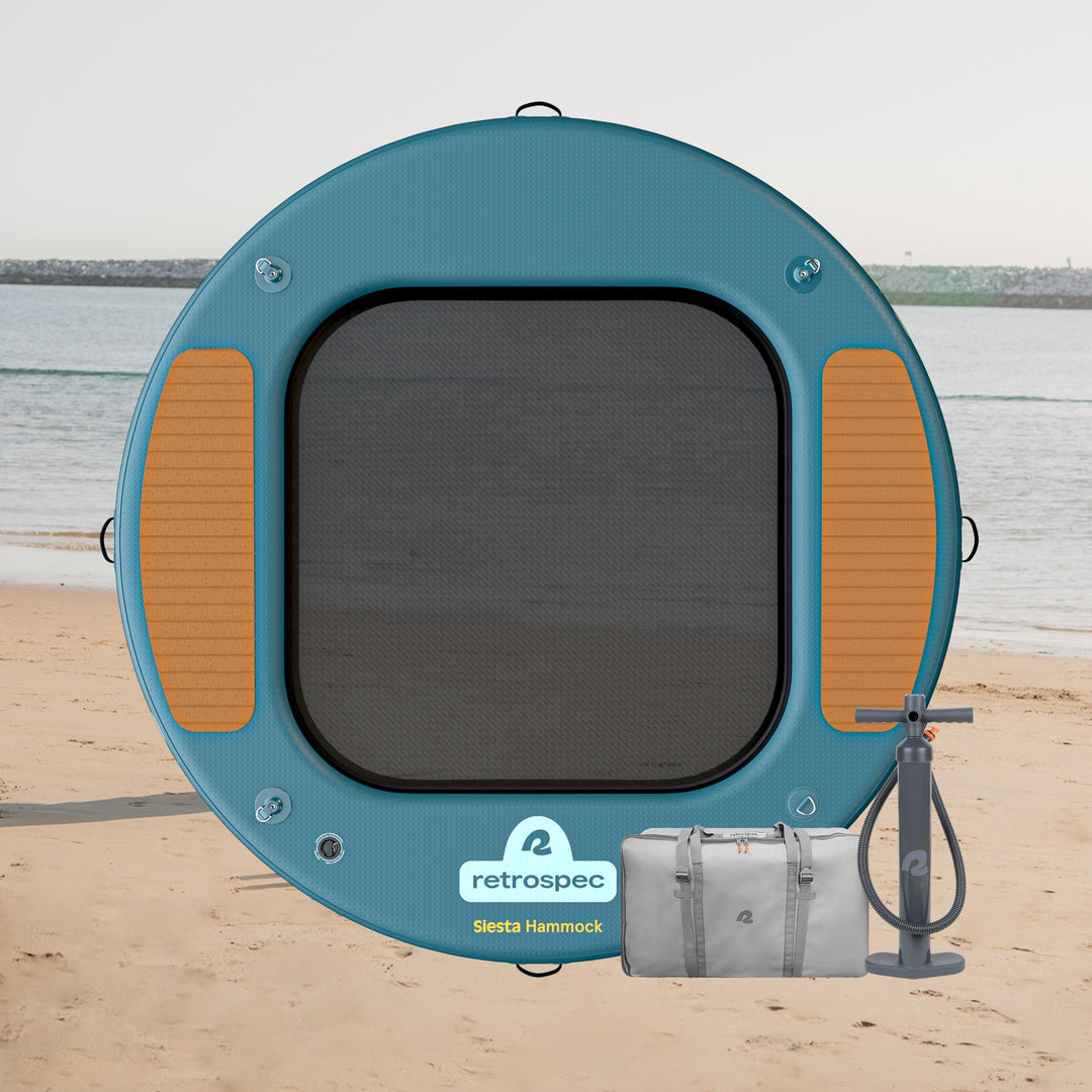A retrospec Siesta Hammock on the beach, featuring a mesh center and textured side panels, alongside a pump and carrying bag.