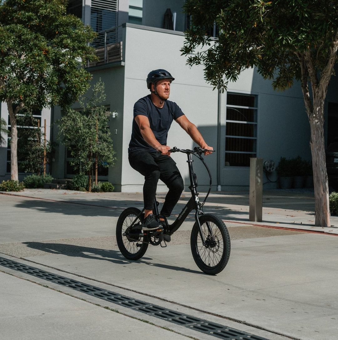 Man riding black retrospec Judd Rev urban electric bike on city pavement with modern buildings