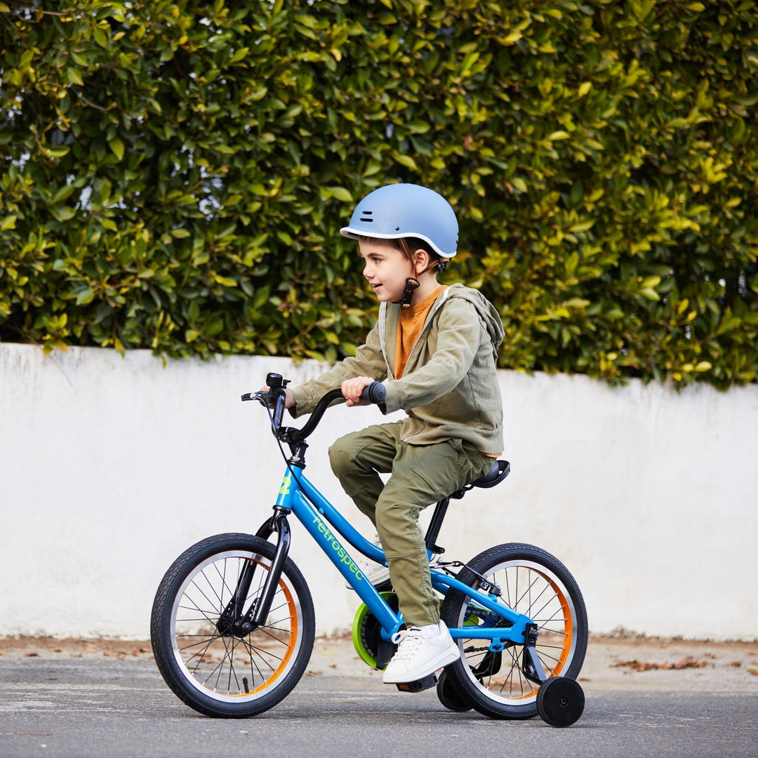 young boy riding a blue retrospec 16 inch kids bike with training wheels on a sidewalk