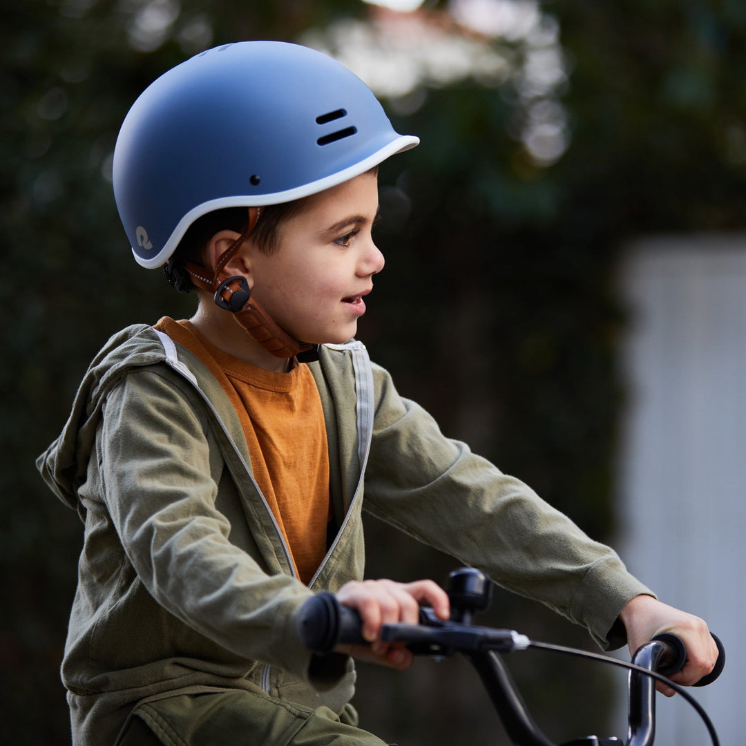 Child riding a kids bike outdoors on a sunny day wearing safety gear.
