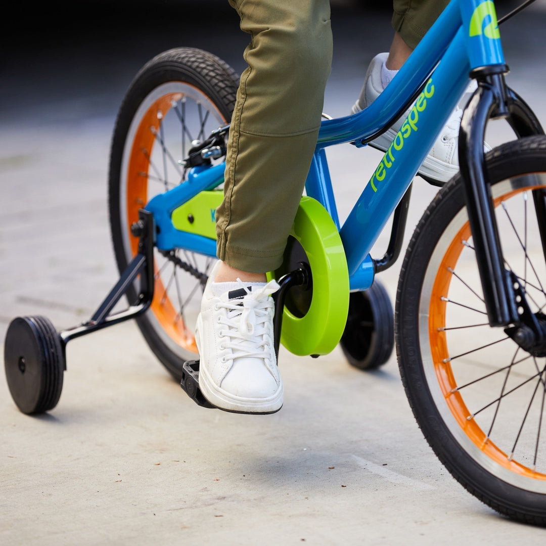 Child's foot on retrospec Koda pedal with blue frame and lime-green training wheel hub in close-up