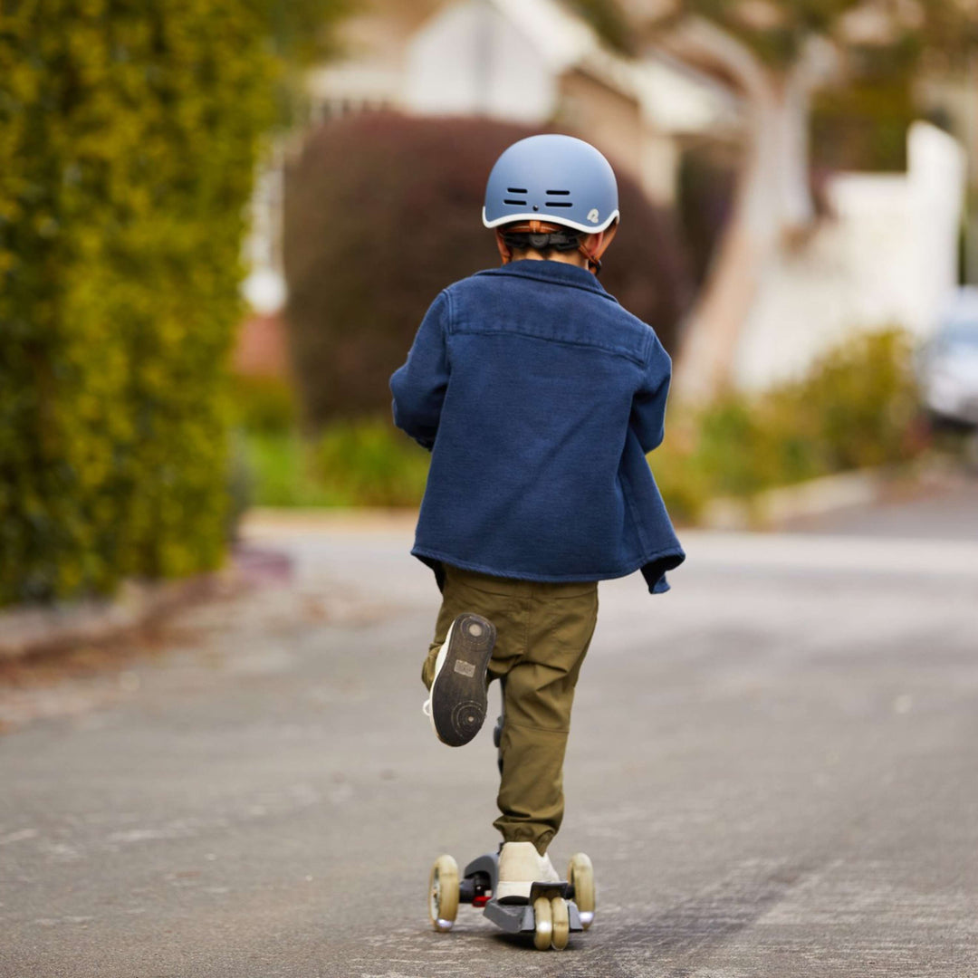 Young child riding a three-wheel kids scooter on a smooth sidewalk path