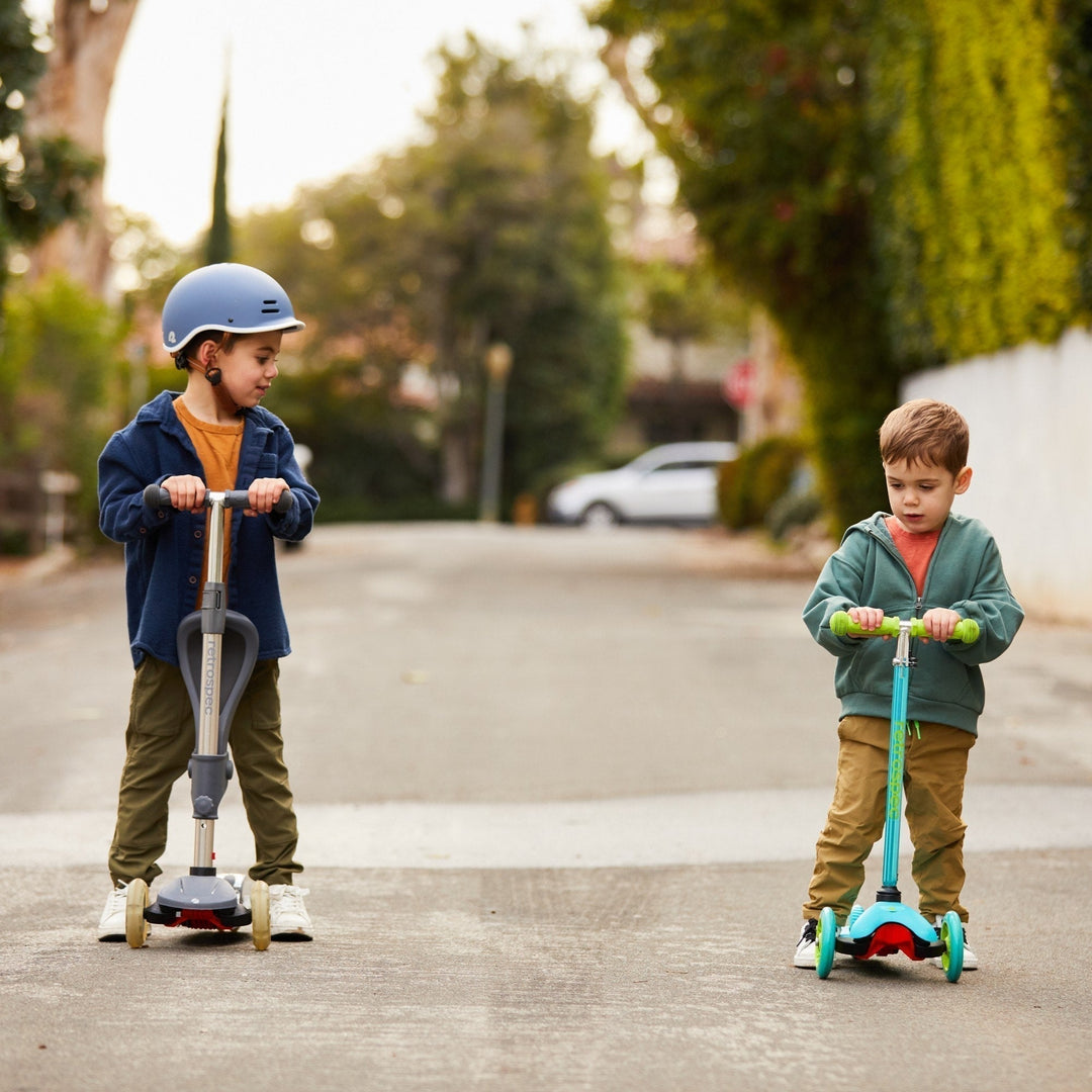 Two young children ride scooters down a quiet street.