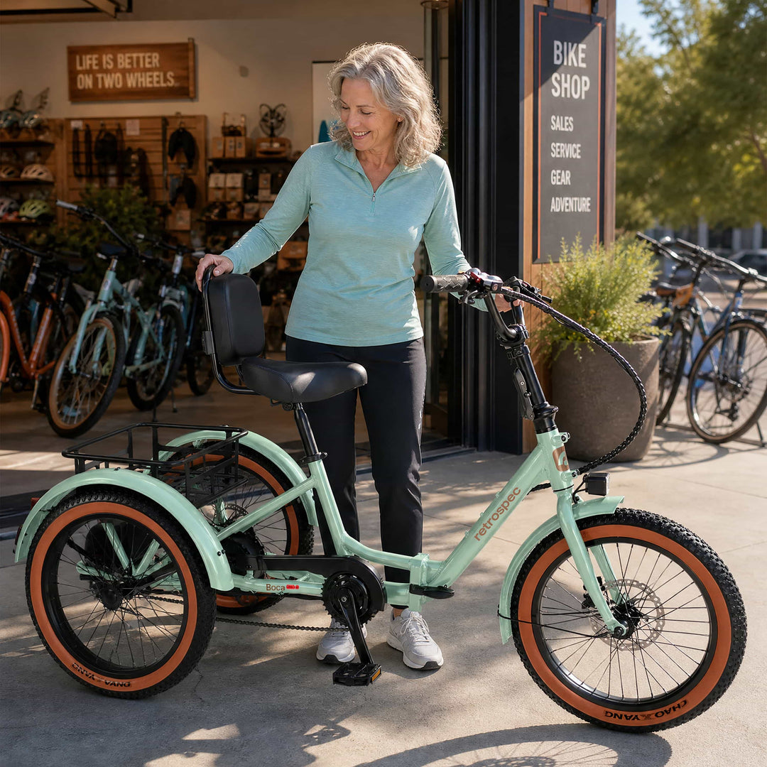 Woman admiring a mint green retrospec Boca Rev Electric Trike with brown-wall tires on display inside a bike shop.