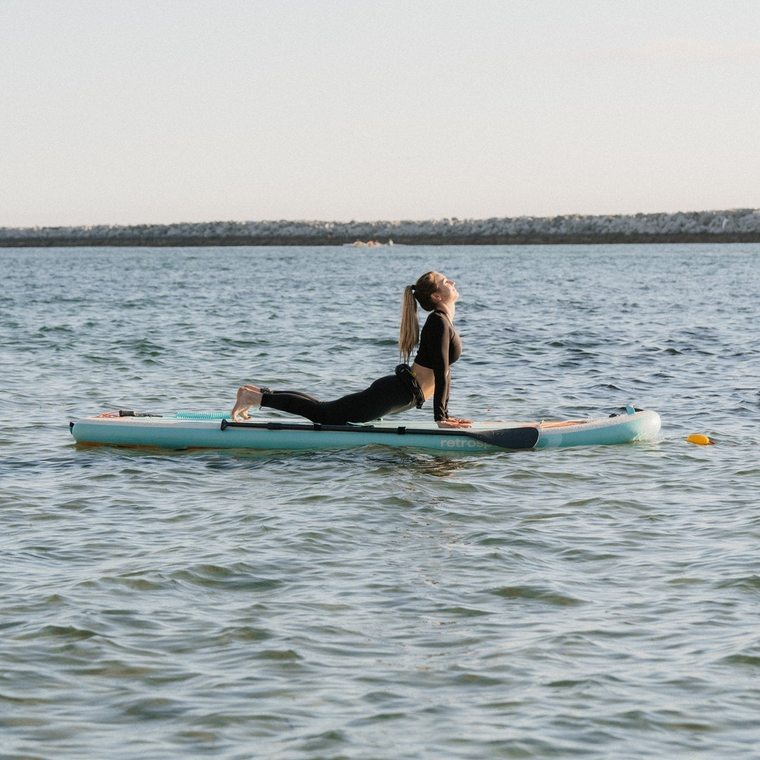 Person does a yoga position on an inflatable paddle board on the water.