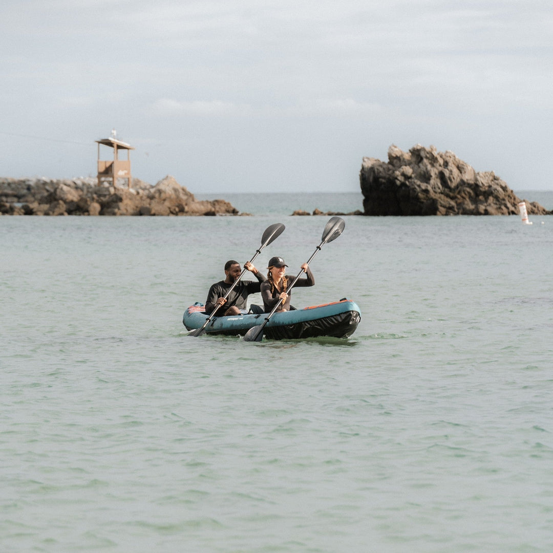 Two paddlers on teal retrospec Coaster tandem kayak in ocean with rocky islands and scenic coastline