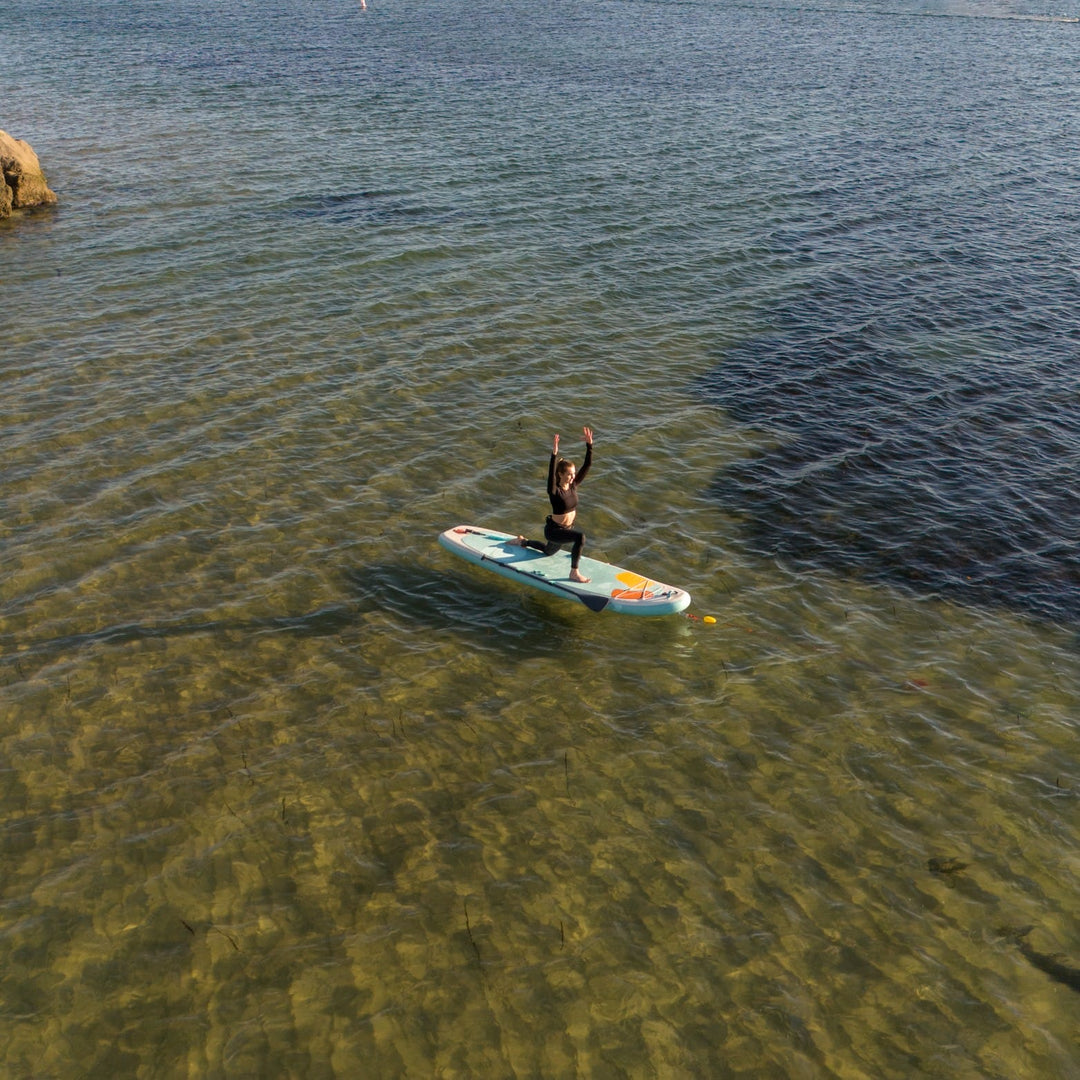 A woman does yoga on an inflatable paddle board in calm water.