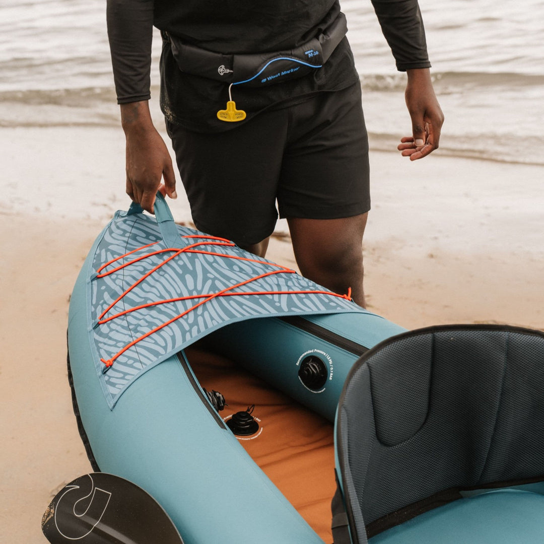 Light blue retrospec Coaster inflatable kayak with red sail rig and orange interior visible on beach