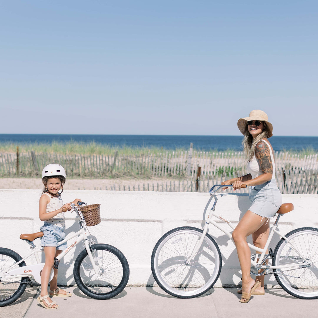An adult and child face eachother while sitting on their white beach cruiser chatham bikes.