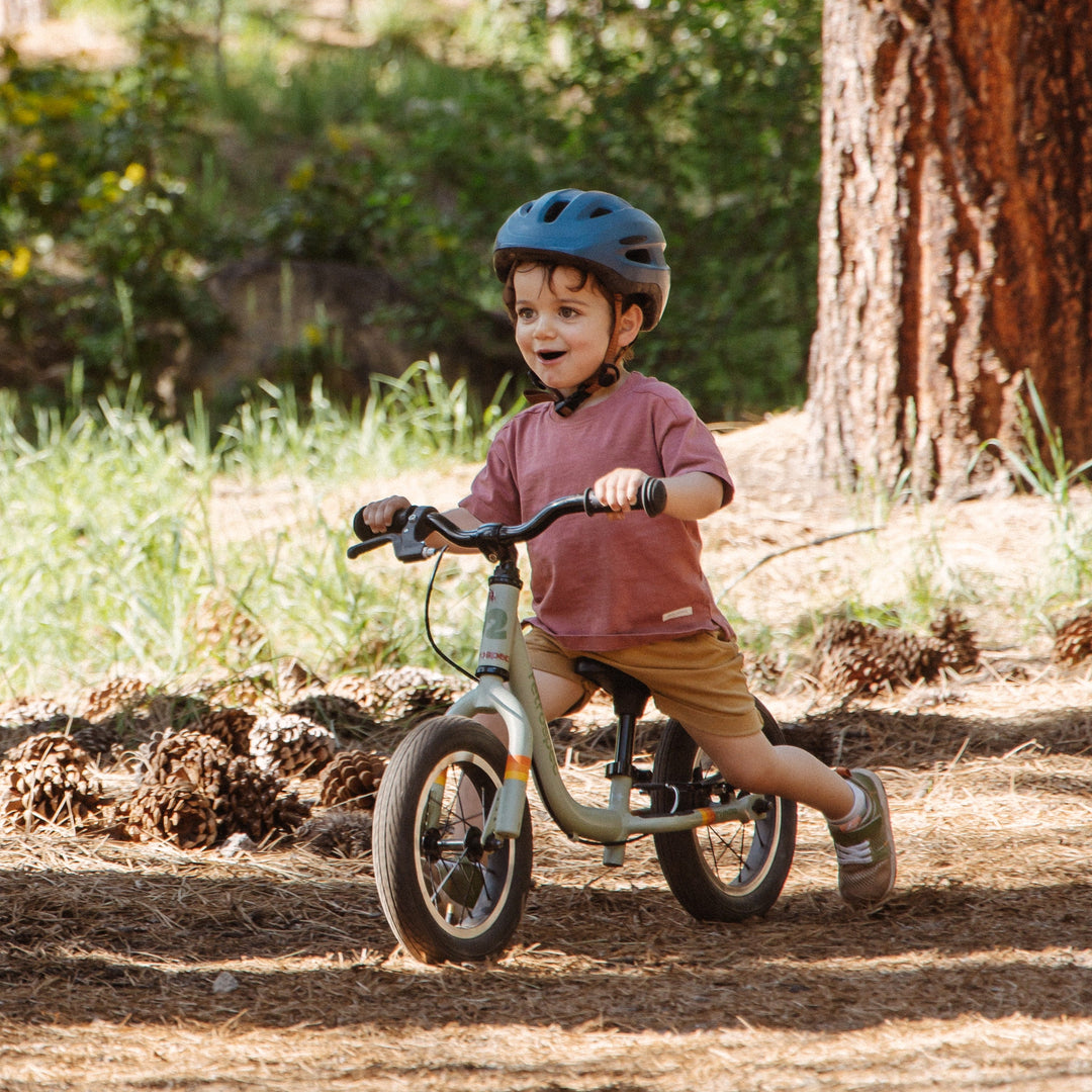 Toddler riding retrospec Cub Plus 12 push bike on dirt trail with blue helmet