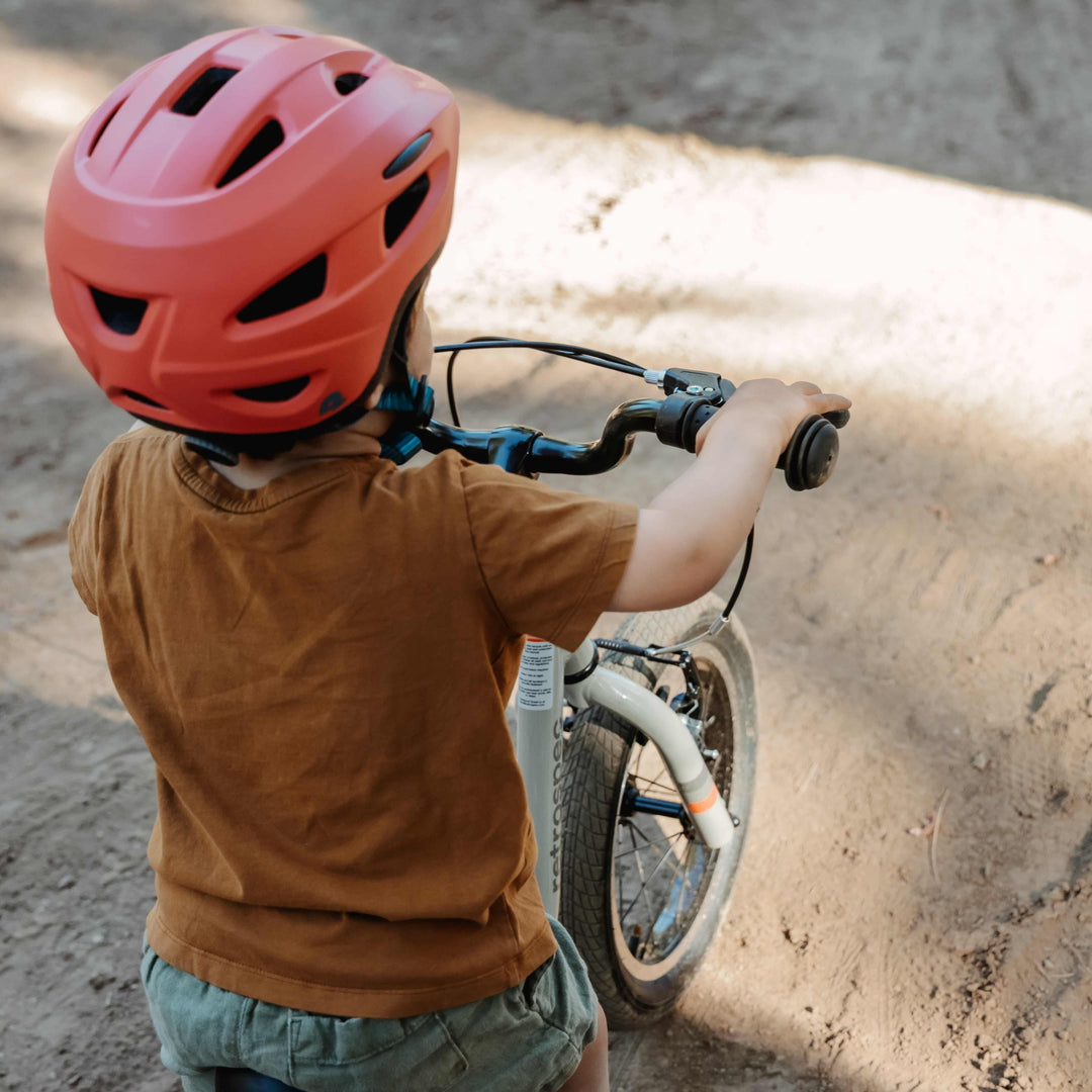 A young child wearing an orange helmet rides their balance bike on a dirt path.
