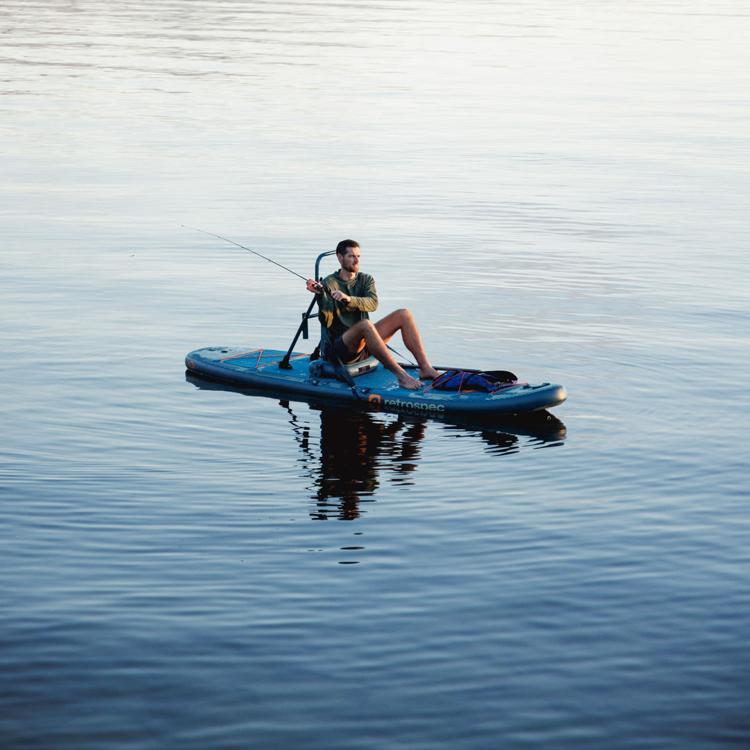 retrospec June inflatable fishing paddle board with rod holders and deck storage on the water.