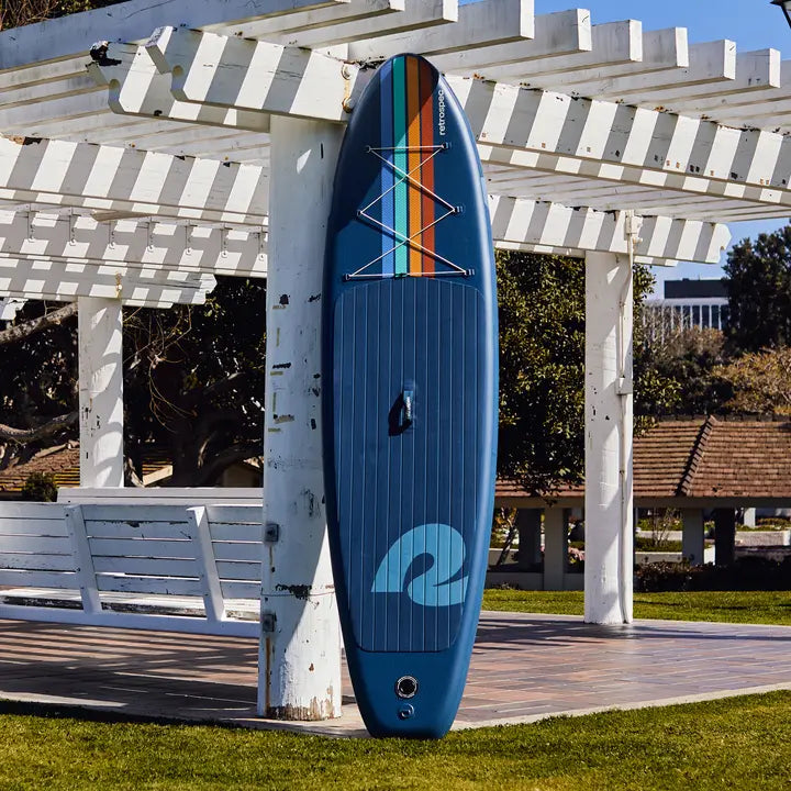 retrospec Weekender 10 foot paddle board in dark blue with colored bracing, displayed against outdoor pergola structure.