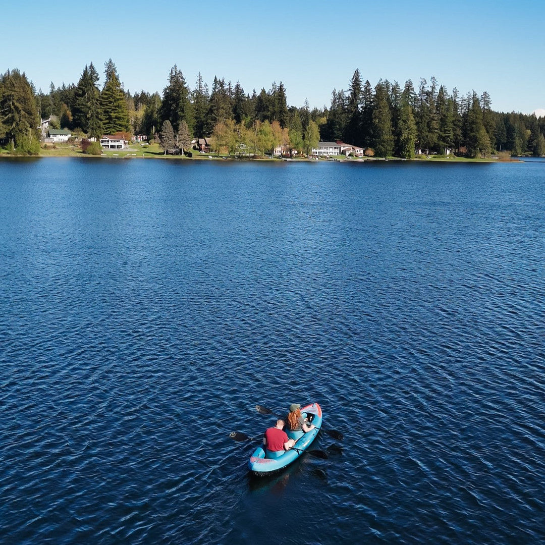 Couple paddling an inflatable kayak together on a calm lake.