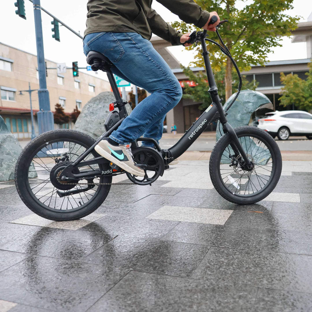 Rider on a retrospec Judd Rev Folding Electric Bike navigating a wet city sidewalk.