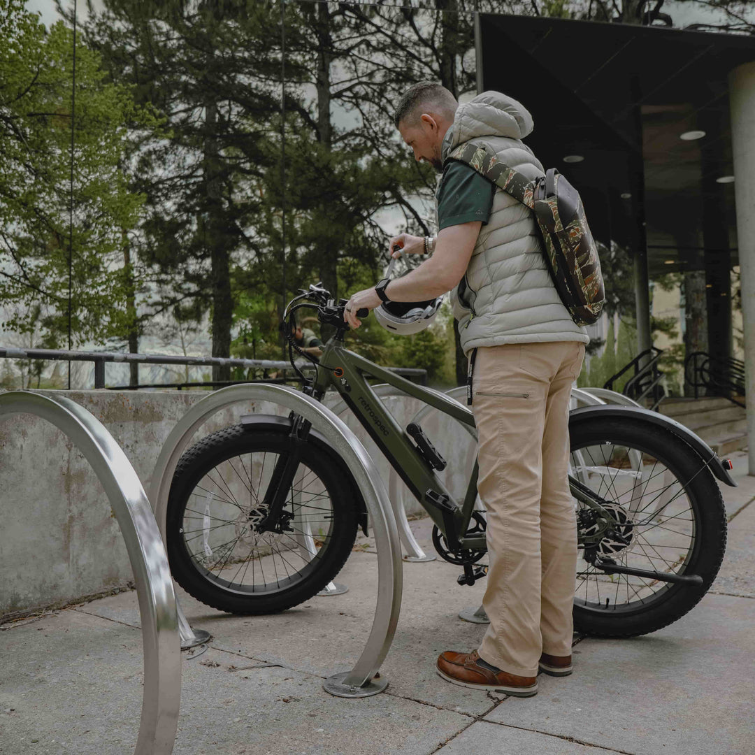 Man with a backpack standing next to a retrospec fat tire EBike on a campus path with a historic building in the background.