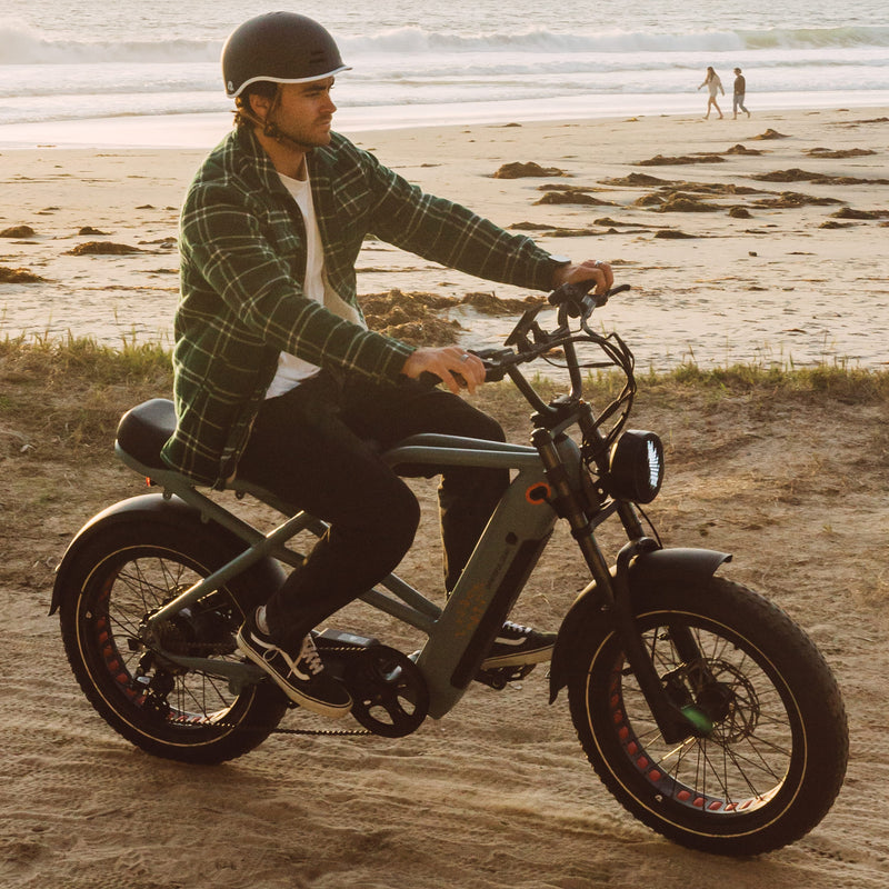 A person rides an electric bike along a sandy beach with gentle waves in the background, showcasing a relaxed outdoor atmosphere.