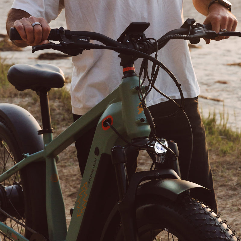 A person in a white shirt grips the handlebars of a green electric bike, showcasing its modern design.