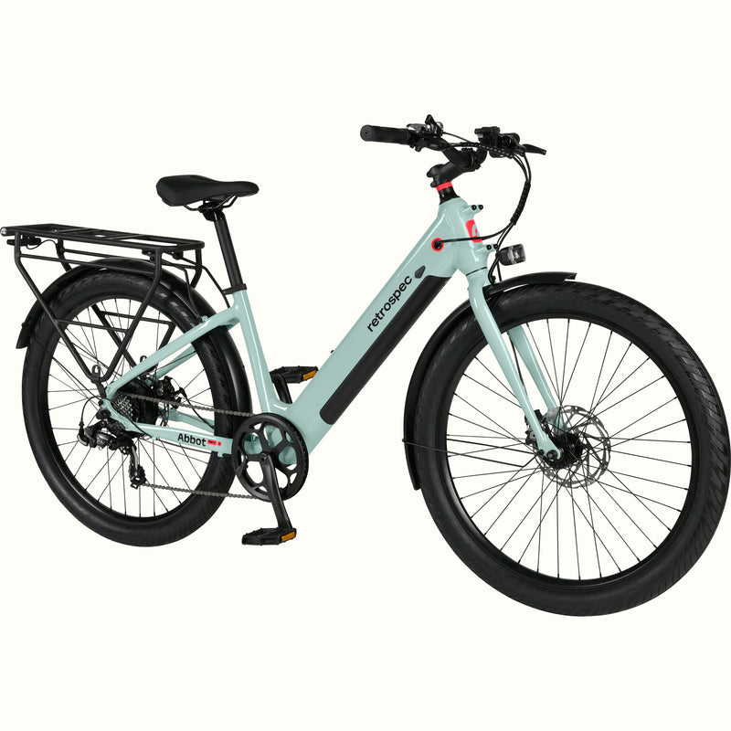 A modern, sleek Abbot Rev 2 Step Through electric bike in light greenish blue with a low step-through frame, wide tires, and a rear rack, branded "retrospec."