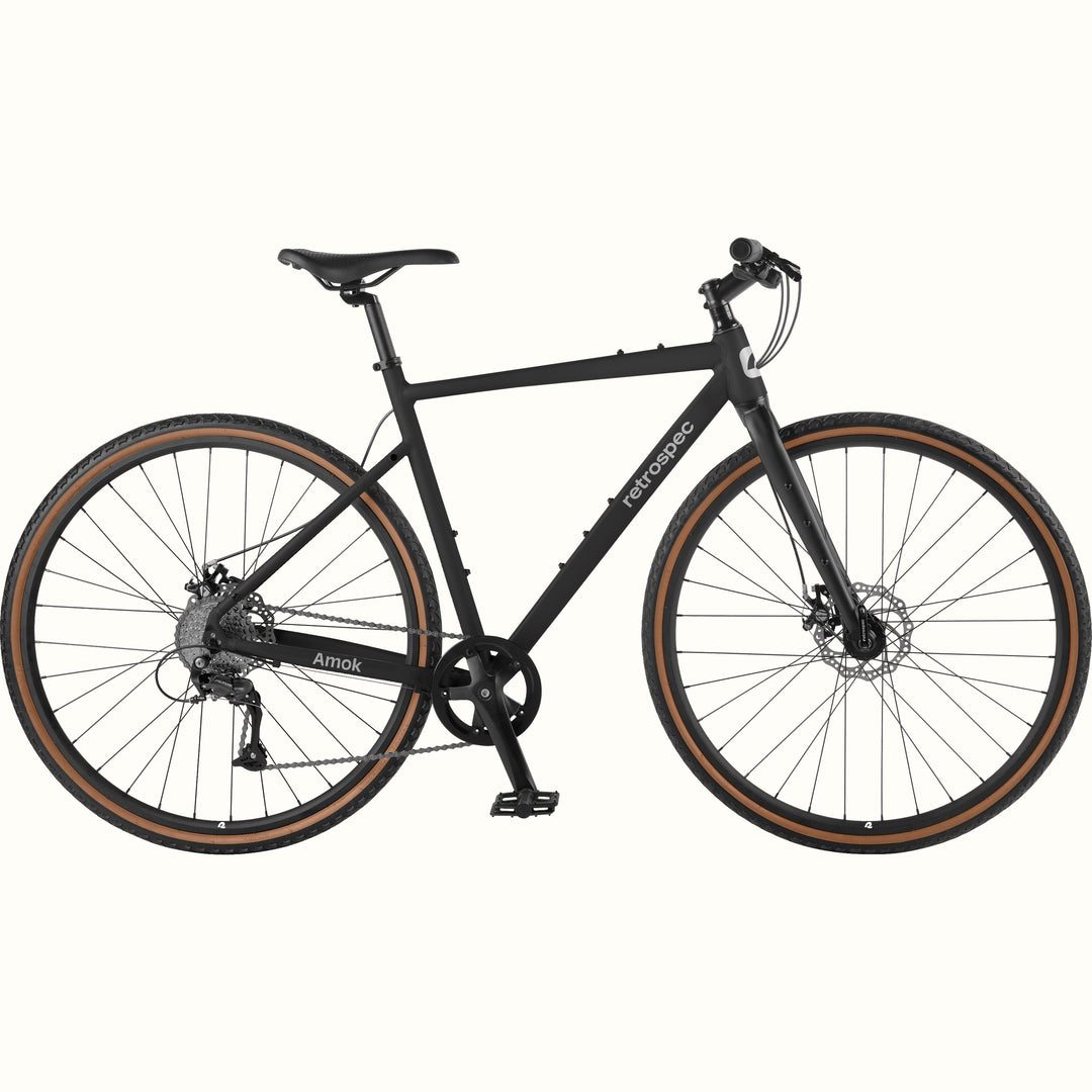 retrospec Amok matte black gravel bike with tan wall tires, disc brakes, and flat bar, shown in full side profile.