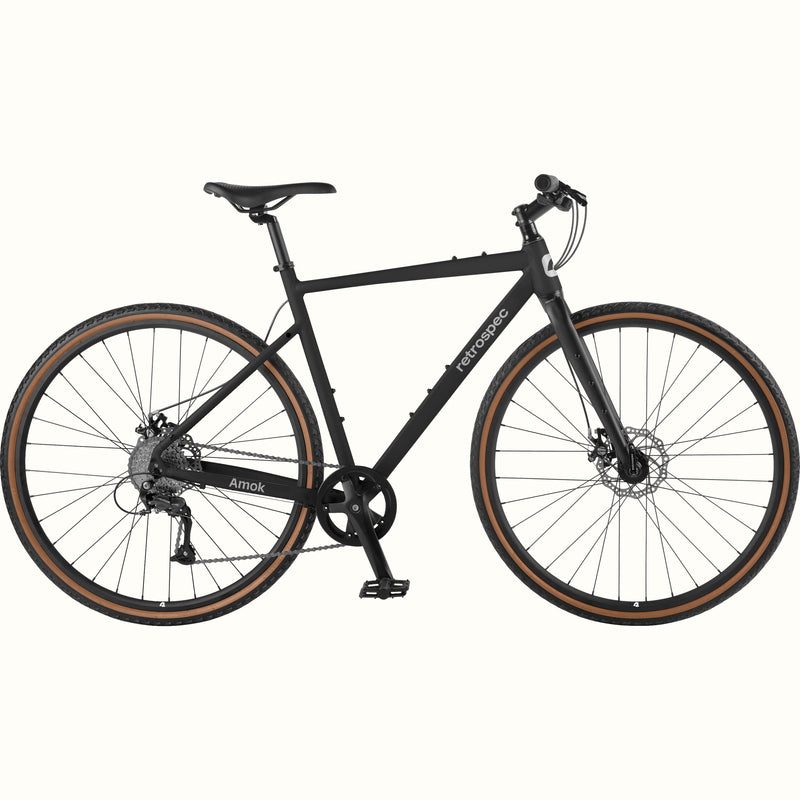 retrospec Amok matte black gravel bike with tan wall tires, disc brakes, and flat bar, shown in full side profile.