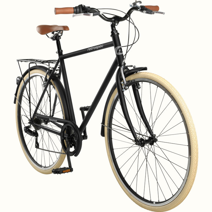 A black city bicycle with tan leather-look saddle and grips, tan sidewall tires, and brown handlebar grips, photographed on a plain light background.