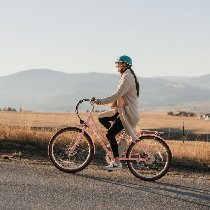 Person riding a Beaumont Rev 3 City Electric Bike - Step Through on a road with mountains in the background.
