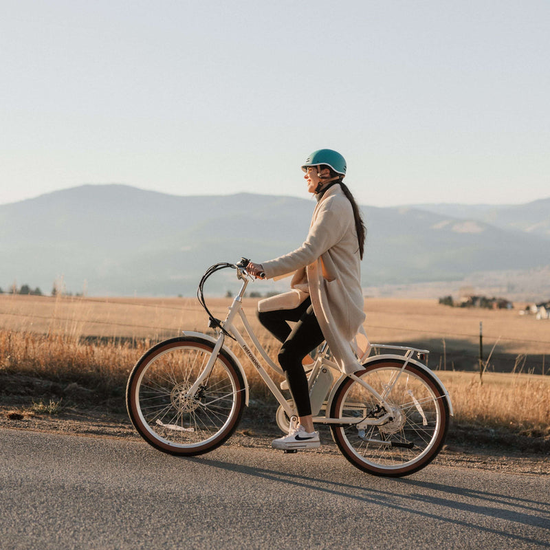 Person riding a Beaumont Rev 3 City Electric Bike - Step Through on a road with mountains in the background.