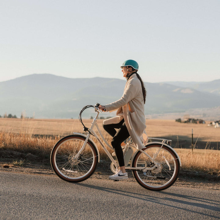 Person riding a Beaumont Rev 3 City Electric Bike - Step Through on a road with mountains in the background.
