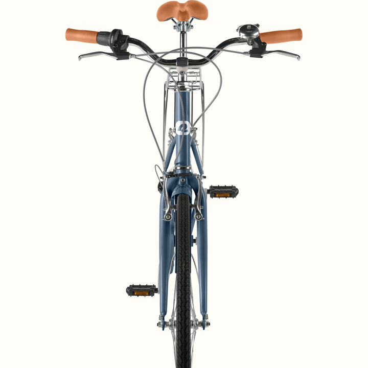 Font view detail of retrospec Beaumont ST urban bike handlebars with bell, brown leather grips, front rack, and dusk blue fork.