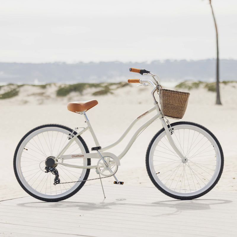 retrospec Chatham beach cruiser bike with wicker basket parked on a boardwalk near sand dunes.
