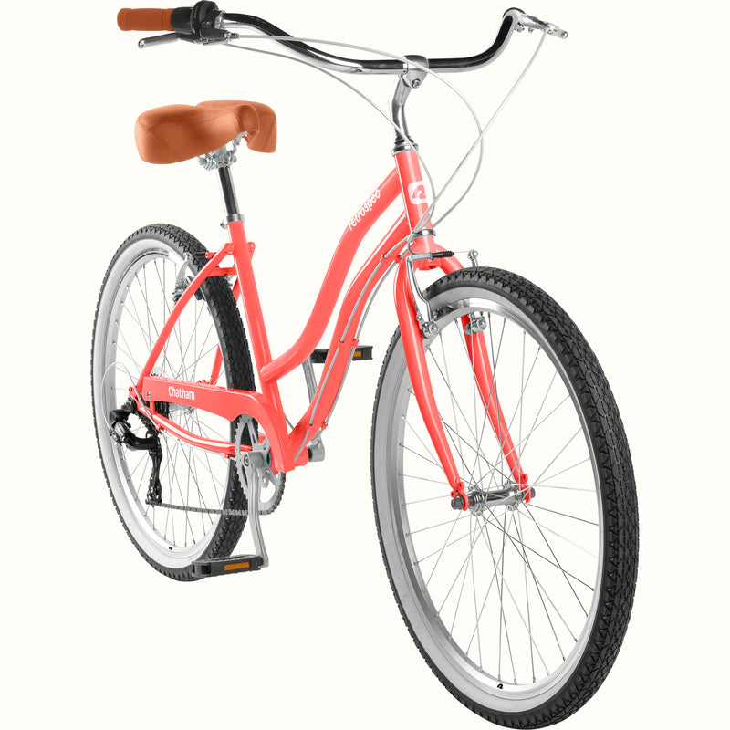 retrospec Chatham 7 speed cruiser bike in coral pink, shown from a front three-quarter studio angle.