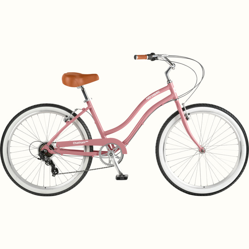 retrospec Chatham Plus women's cruiser bike in dusty rose with 7-speed gearing, white tires, step-through steel frame, and brown leather saddle, side view.