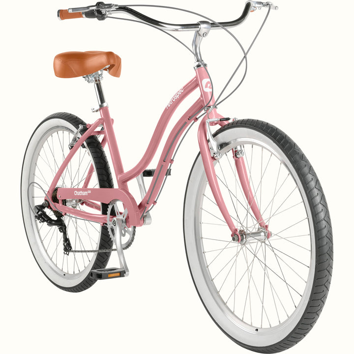 retrospec Chatham Plus 7 speed cruiser bike in dusty rose, three-quarter view showing rear derailleur, hand brakes, white rims, and brown leather saddle.