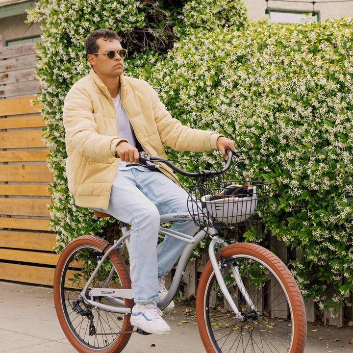 Person in a yellow jacket riding a bicycle next to flowering shrubs.