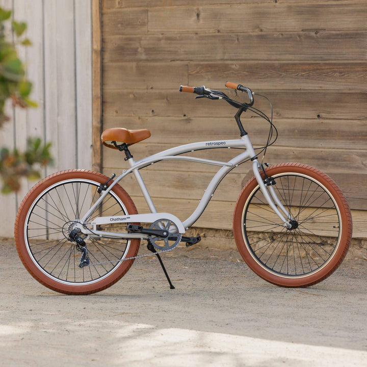 A silver beach cruiser bicycle with brown tires in front of a wooden wall.