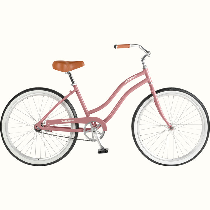 retrospec Chatham Plus beach cruiser bike in dusty rose with white tires, brown leather saddle, and classic step-through frame, side view.