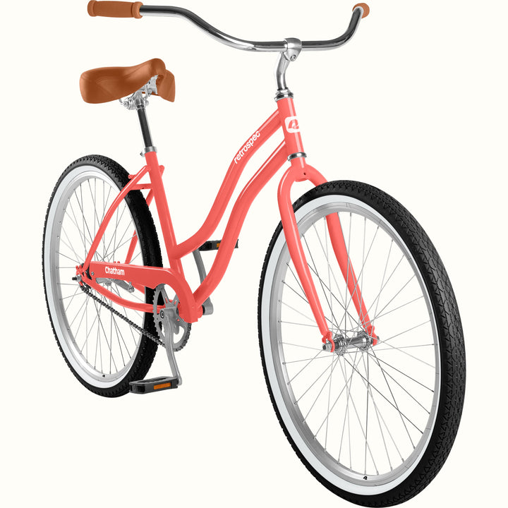 A step-through cruiser bicycle with a coral pink frame, brown leather saddle and handlebar grips, and black tires with silver rims, shown on a plain light background.