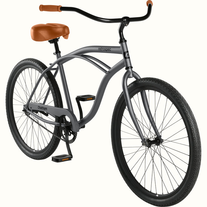 retrospec Chatham beach cruiser bike in matte graphite, angled view showing the curved frame, tan saddle, and chain guard.