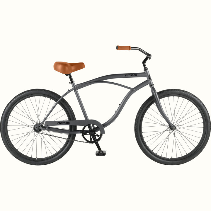 Side profile of the retrospec Chatham cruiser bike in matte graphite with a tan saddle, tan grips, and black tires.