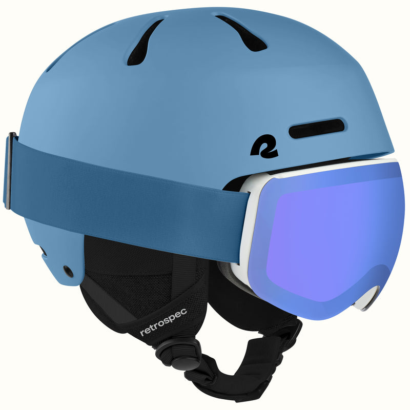 A matte blue ski helmet with a matching blue visor strap and a white-framed ski goggles featuring a blue mirrored lens. The helmet has black vents and a black chin strap with the 'retrospec' brand name visible.