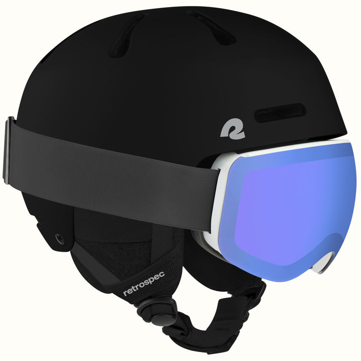 A matte black retrospec ski helmet with a wide black strap and a white-framed ski goggle featuring a blue mirrored lens, shown against a plain off-white background.