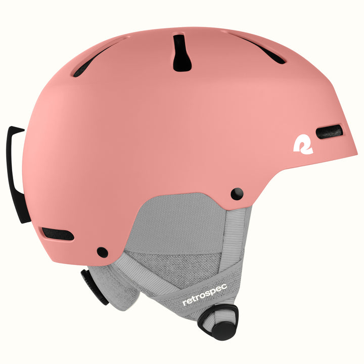 A matte pink ski helmet with a gray chin strap and black ventilation slots, featuring a white 'retrospec' logo on the side and front.