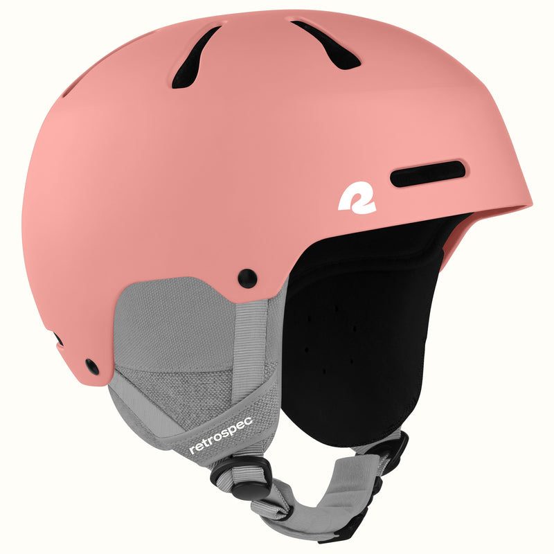 A matte pink ski helmet with gray and black chin straps, featuring a white retrospec logo on the side, set against a plain off-white background.