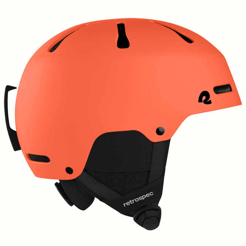 An orange ski helmet with black vents, a black chin strap, and a black logo on the side, shown against a plain off-white background.