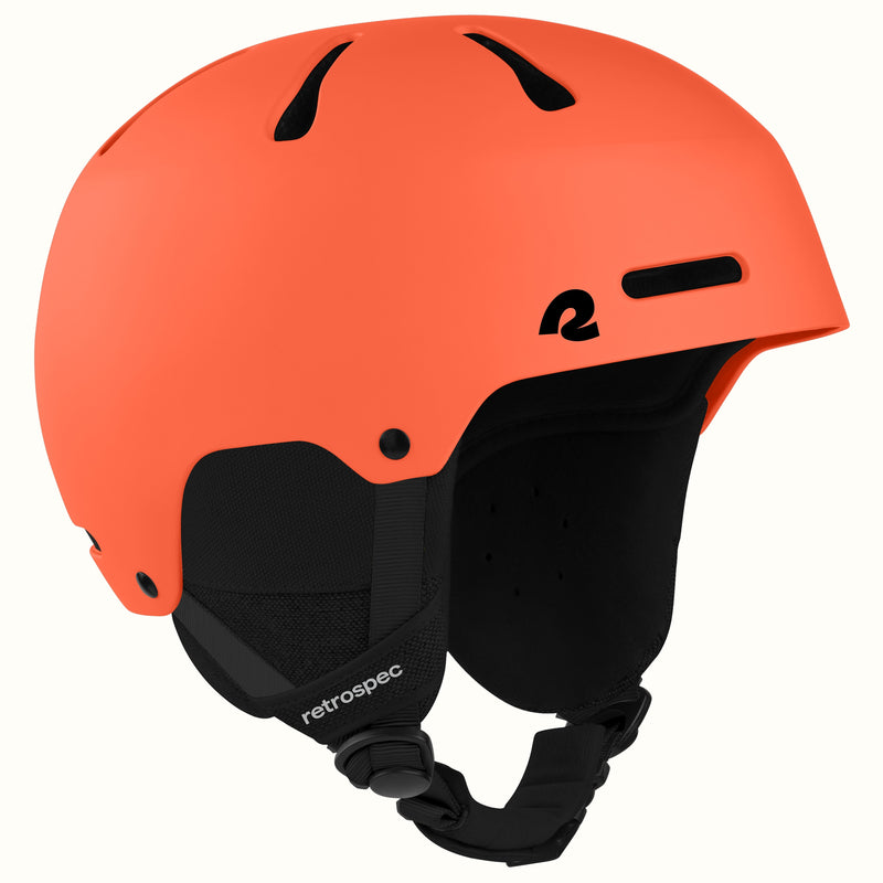 An orange ski helmet with black ventilation slots, a black interior padding, and a black chin strap, shown on a plain off-white background.
